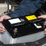 A car mechanic replaces a battery.